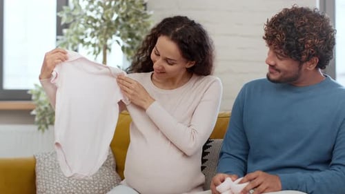 Expectant couple admiring baby clothes at home