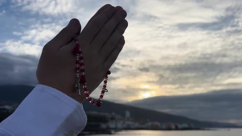 Hands Holding Rosary with Sunset Sky and Island