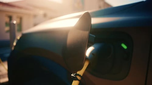 Nahaufnahme eines Ladeanschlusses für Elektrofahrzeuge, der an ein Auto angeschlossen ist, mit warmem Sonnenuntergangslicht und LED-Licht