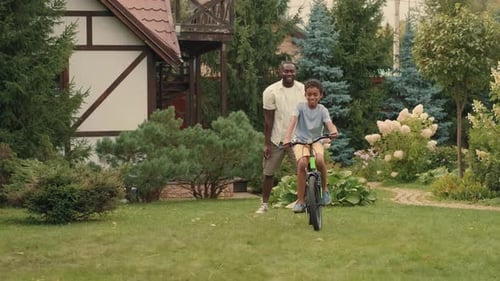 Boy Learns to Ride Bike with Father in Backyard