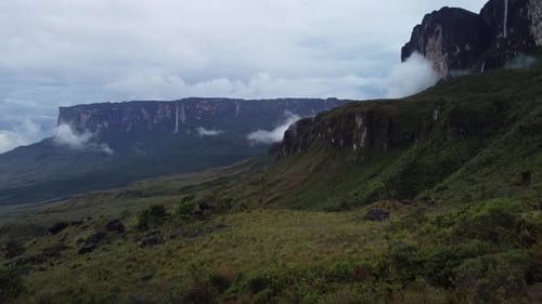 Zumbido sobrevolando la hierba en la base de Roraima Tepuy con cascadas y nubes que lo cubren