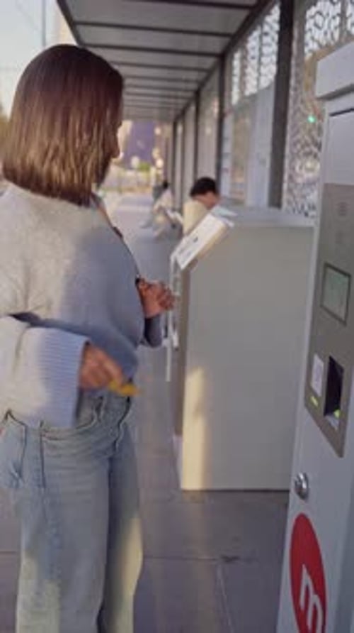 Young commuter woman validating metro ticket at an outdoor automated kiosk