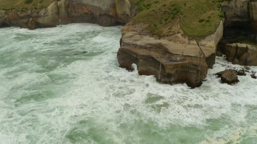 Aerial panning and tilting up shot of cliffs along the coastline with waves hitting the cliff walls
