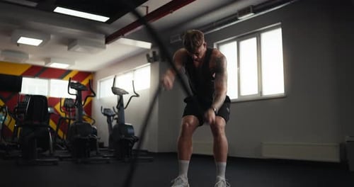 Young Adult Man Exercising with Battle Ropes in Gym