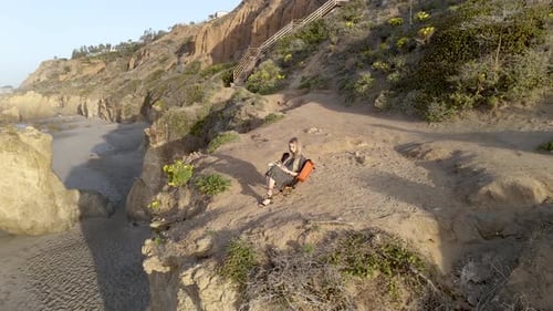 Mujer joven leyendo un libro en lo alto de un acantilado sobre la playa de El Matador, Malibú