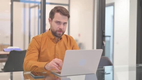 Businessman Looking at Camera while Working on Laptop in Office