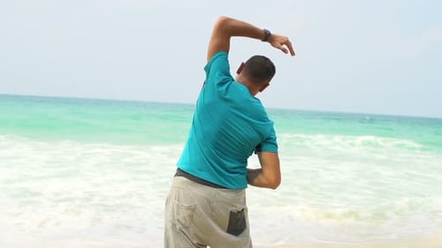 Young man stretching arms on tropical beach warmup in super slow motion