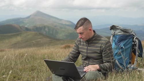 A Man Works at a Computer While Hiking in the Mountains