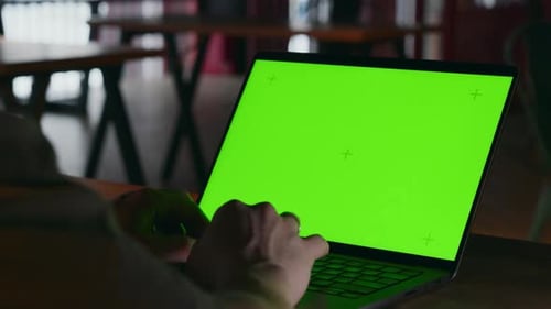 A Green Screen on a Laptop in a Dark Room Where a Man is Working