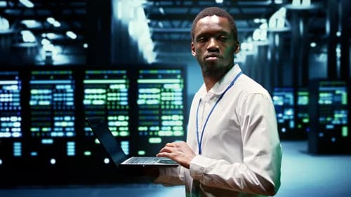 Ingeniero afroamericano inspecciona servidores montados en rack dentro de una instalación de alta tecnología