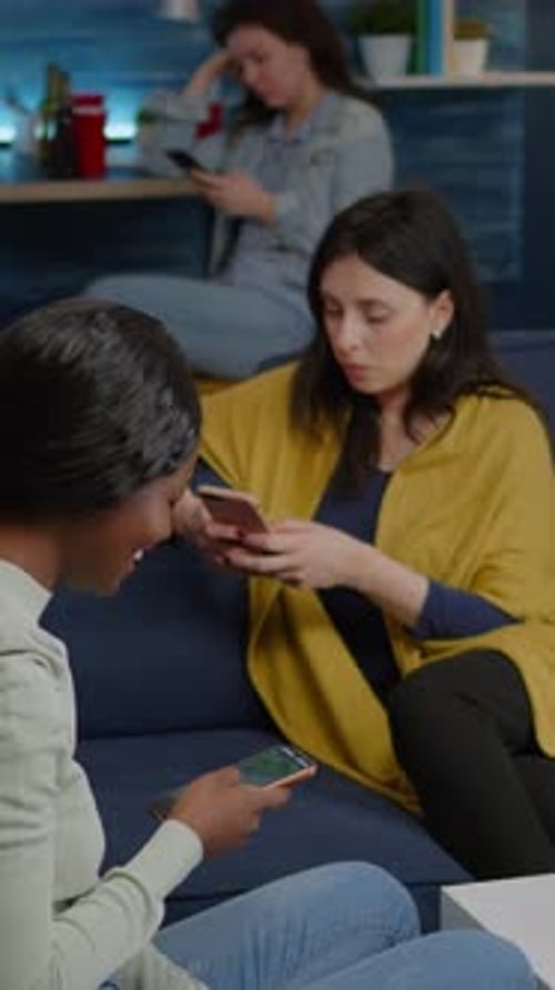 Vertical Video Mixed Race Friends Sitting on Sofa Holdings Mobile in Hands Browsing on Internet