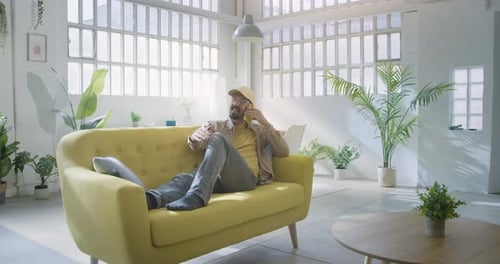Bearded Man Relaxing on Couch Talking on Phone