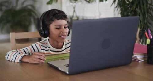 Biracial boy learning online using laptop at table, slow motion