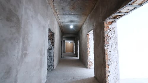 Moving by the long corridor with doorways. A walk in the unfinished building under construction.