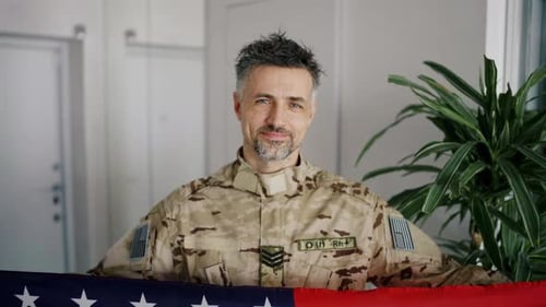 Man in Military Uniform Holding American Flag Indoors