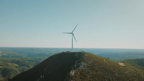 Scenic aerial view of wind turbine on top of a hill. Generating green energy on a cloudless day.