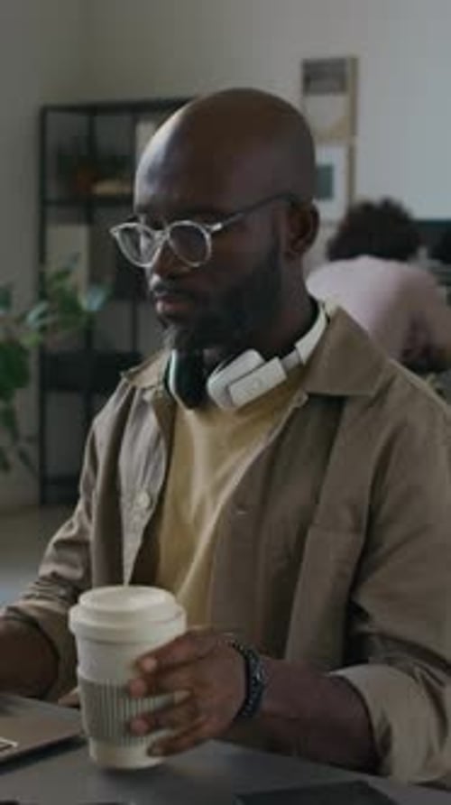 Male Web Engineer Drinking Coffee from Reusable Cup while Working on Laptop