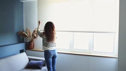 Woman adjusting living room blinds to enhance ambiance and control light