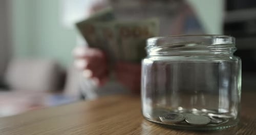 Woman Putting a Roll of Money in a Glass Jar Family Saving Money Money Box