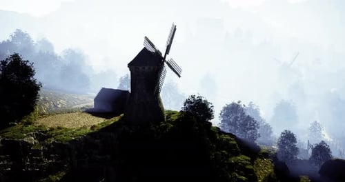 Historic Windmill Stands on a Hill Among Trees in Early Morning Mist