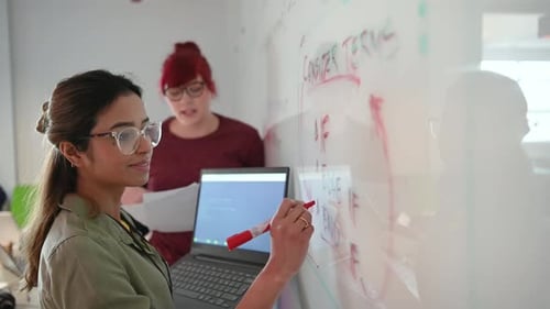 Women brainstorming and writing on whiteboard in office