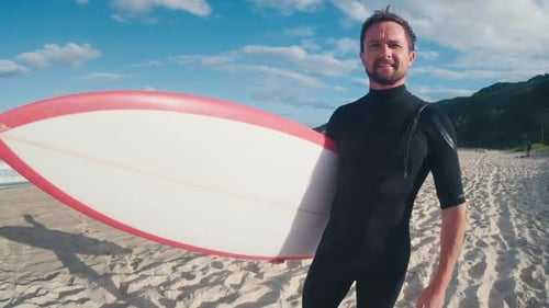 Surfer with board. Male caucasian surfer in black wetsuit stands on the beach