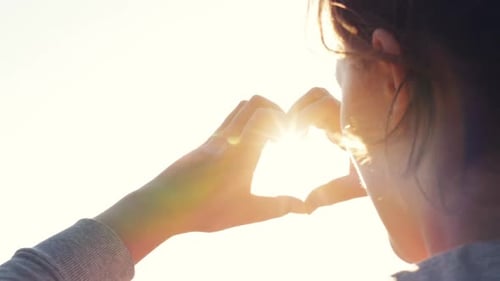 Woman Creates Heart Shape with Hands at Sunset