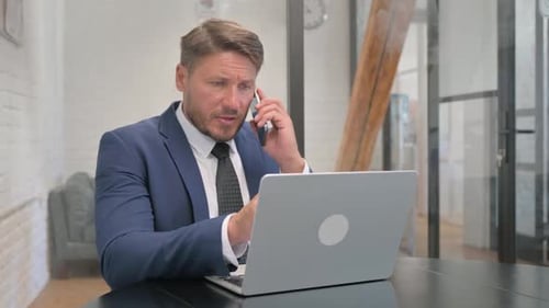 Professional Man Talking on Phone While Using Laptop