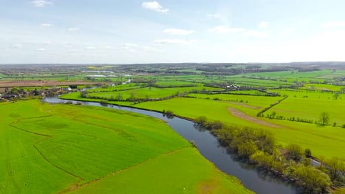 Mäandrierender Fluss, der durch leuchtend grüne Weiden mit Bäumen entlang von Wasserrändern und offenen Feldern fließt
