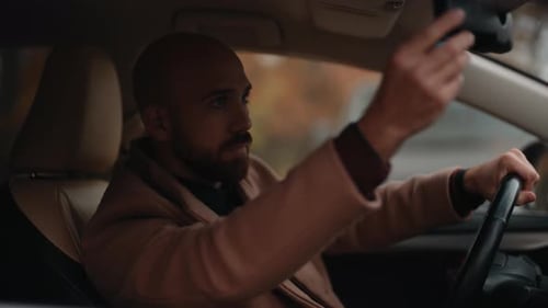 Focused Man Adjusts Rearview Mirror While Sitting in a Modern Car, Preparing for Drive