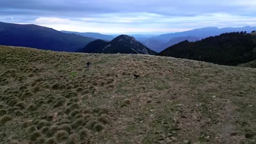 Drone shot of a woman running with her dog at a mountain range while the drone circles around them