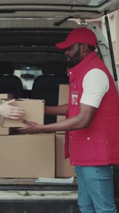 Courier African American Gives a Parce to a Woman After Signing on Delivery Device Near Car