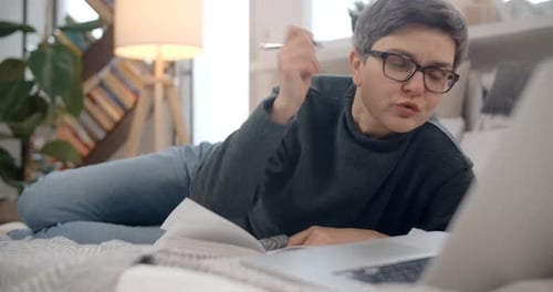 Woman Talks and Writes on Bed With Laptop
