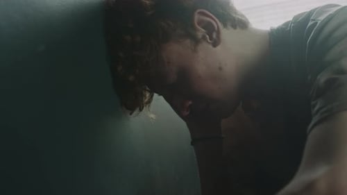 Desperate Young Man Punching Dark Wall with Fist and Pushing with Palm