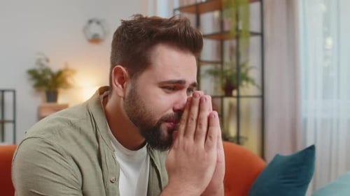 Worried Man Sits with Clasped Hands on Couch