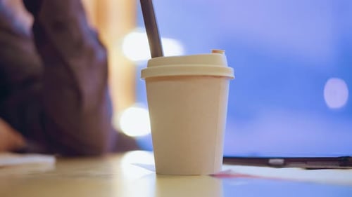 Tasse à café à emporter avec paille posée sur la table à l'intérieur à côté du smartphone et du mouchoir