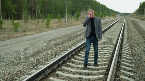 Contemplative Man in Grey Suit Walking Along Railway Tracks in Forest