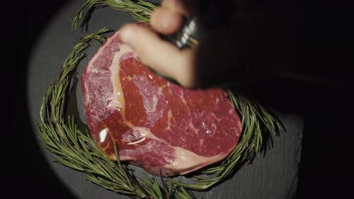 Close-up of steak and rosemary spinning in the spotlight. Close-up, top view, sprinkled with spices.