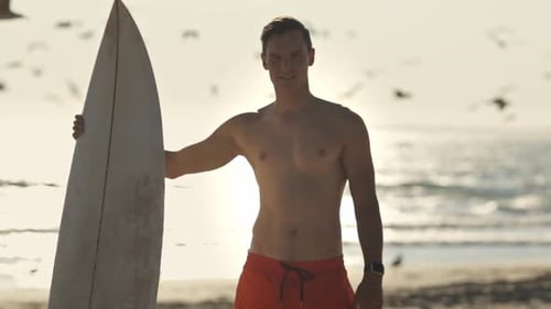 Surfer Holding Surfboard Smiling at Sunset on Beach