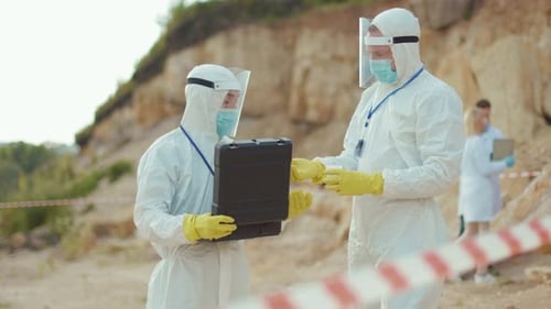 Scientists in Protective Gear Handling Sample Vial Outdoors