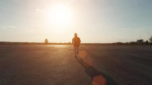 Hombre con capucha negra y pantalones blancos corriendo al aire libre por la noche