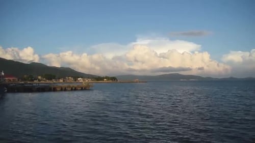 Time lapse of Fluffy Clouds by the Pier with Green Mountains in Background