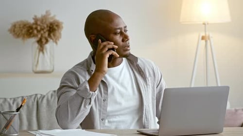 Afroamerikanischer Mann, der während der Arbeit im Home Office telefoniert