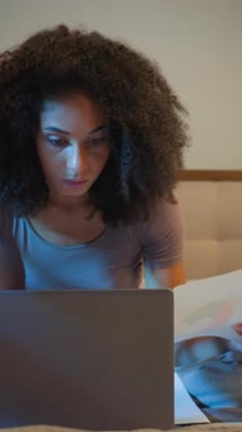 Une femme d'affaires afro-américaine concentrée travaille avec un ordinateur portable et des papiers au lit la nuit Date limite