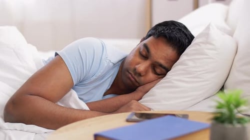 Man sleeping in bed reaches for his phone
