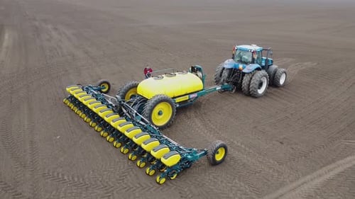 Blue tractor with yellow seeder working on the field in Ukraine OA