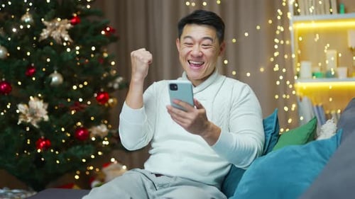 Excited Adult Uses Cell Phone Near Christmas Tree
