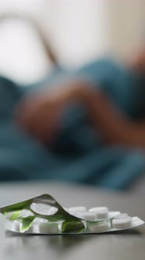 Man Lying in Bed with Pills on Table