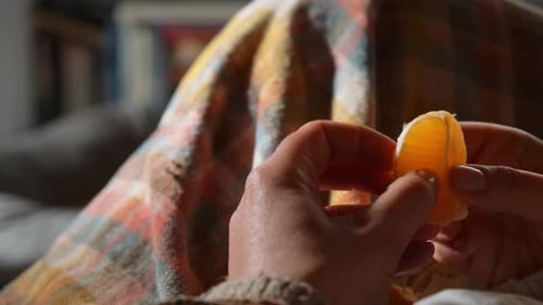 Plan rapproché d'une femme mangeant une mandarine dans un environnement intérieur douillet avec un plaid en tartan