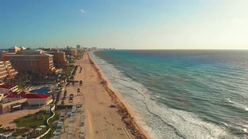 Tropical sea waves crashing on white sandy shore with a blue sky, golden sun rays shine on turquoise